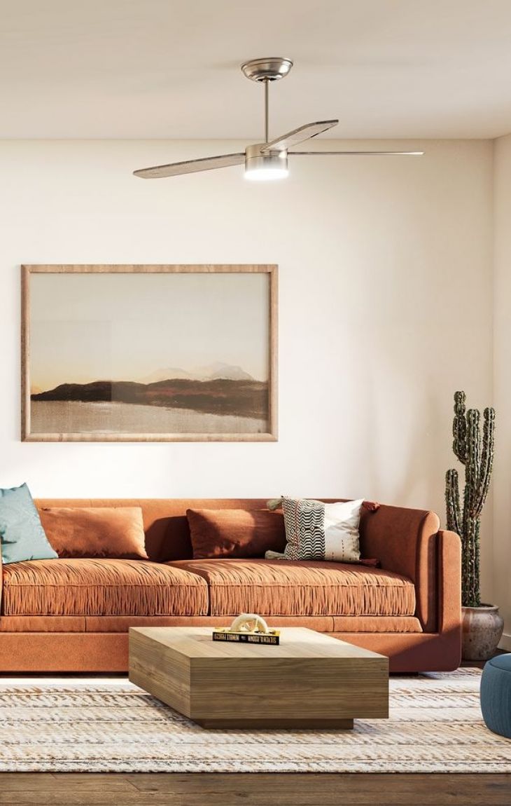 Modern living room with a rust-colored sofa, a cactus, wooden table, and landscape art on the wall.