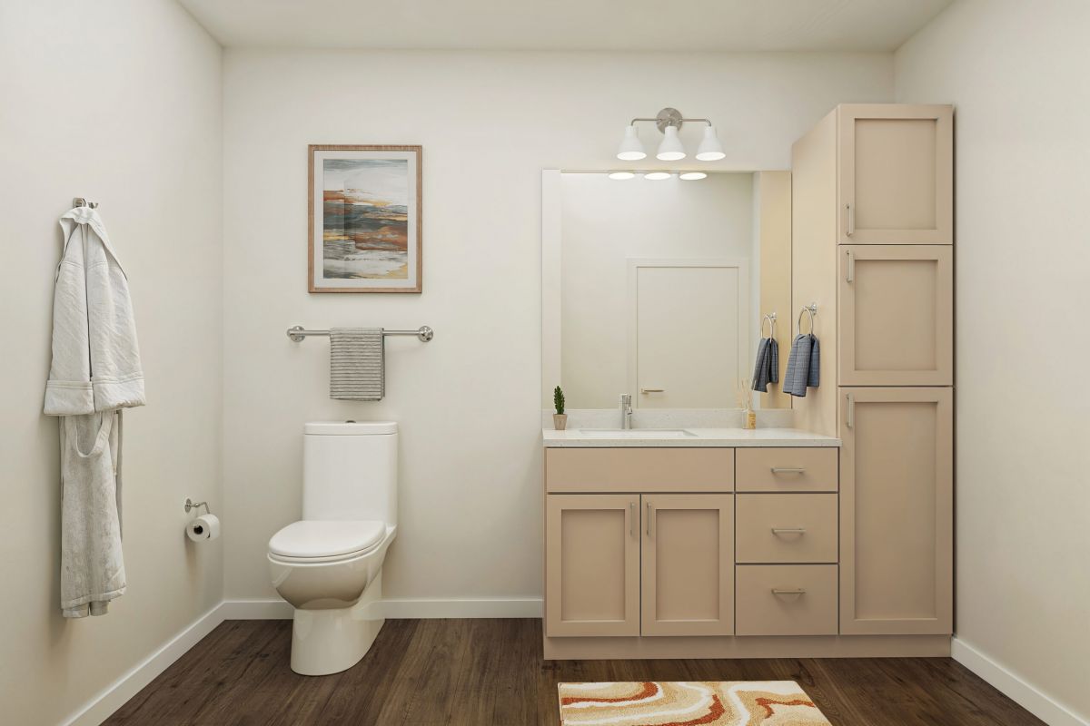 Modern bathroom with beige cabinets, white toilet, towel racks, wall art, and a striped rug on wood flooring.