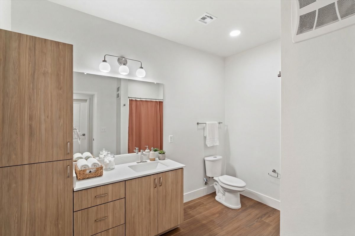 Modern bathroom with wood cabinets, a large mirror, white toilet, and a pink shower curtain.