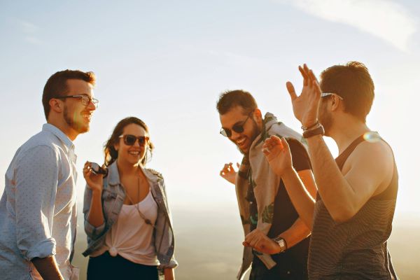 Four friends outdoors laughing and talking together on a sunny day.