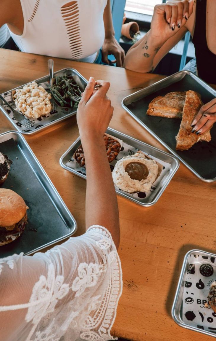 Four people eating assorted meals at a wooden table in a casual restaurant setting, seen from above.